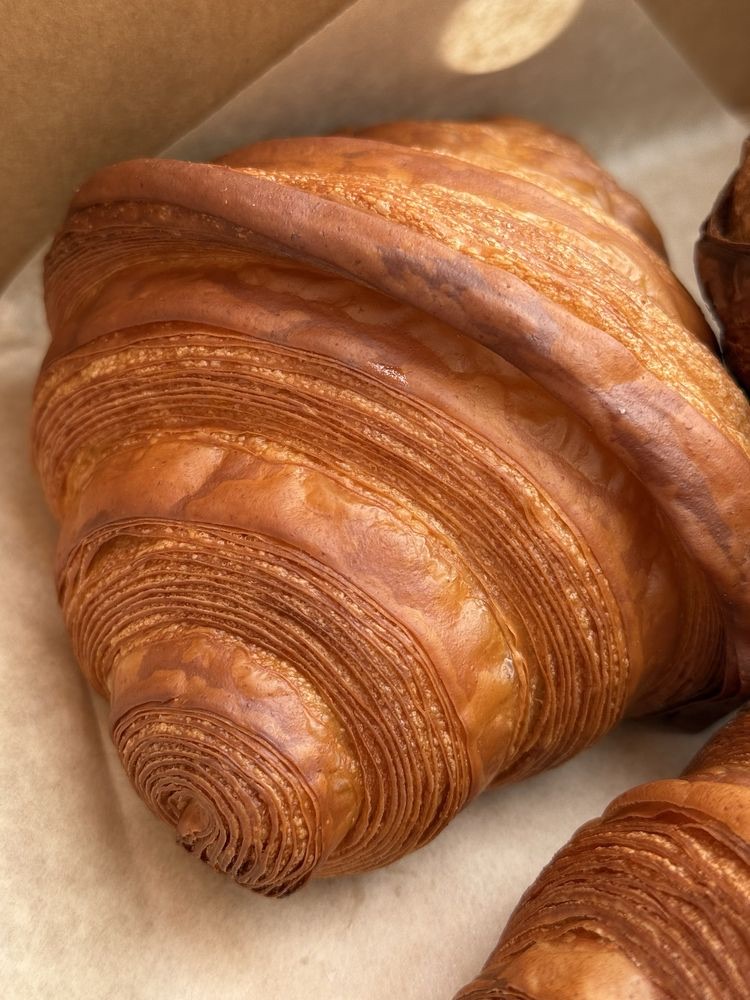 Croissant in a kraft box, in closeup, its thin laminated layers shining