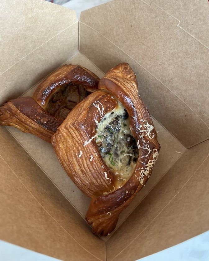 Mushroom bechamel danish topped with shaved cheese, in a kraft to-go box