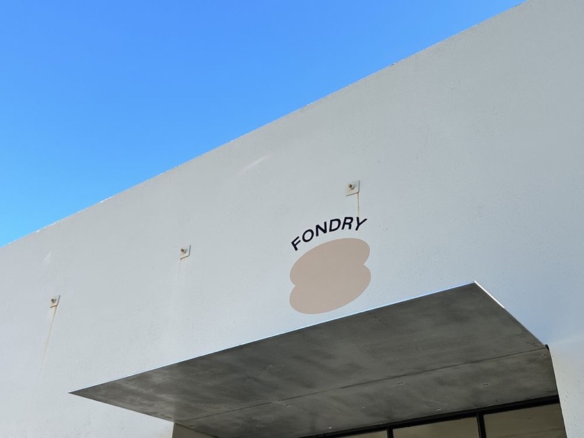White modern storefront with the round Fondry logo painted above the entrance, under a blue sky
